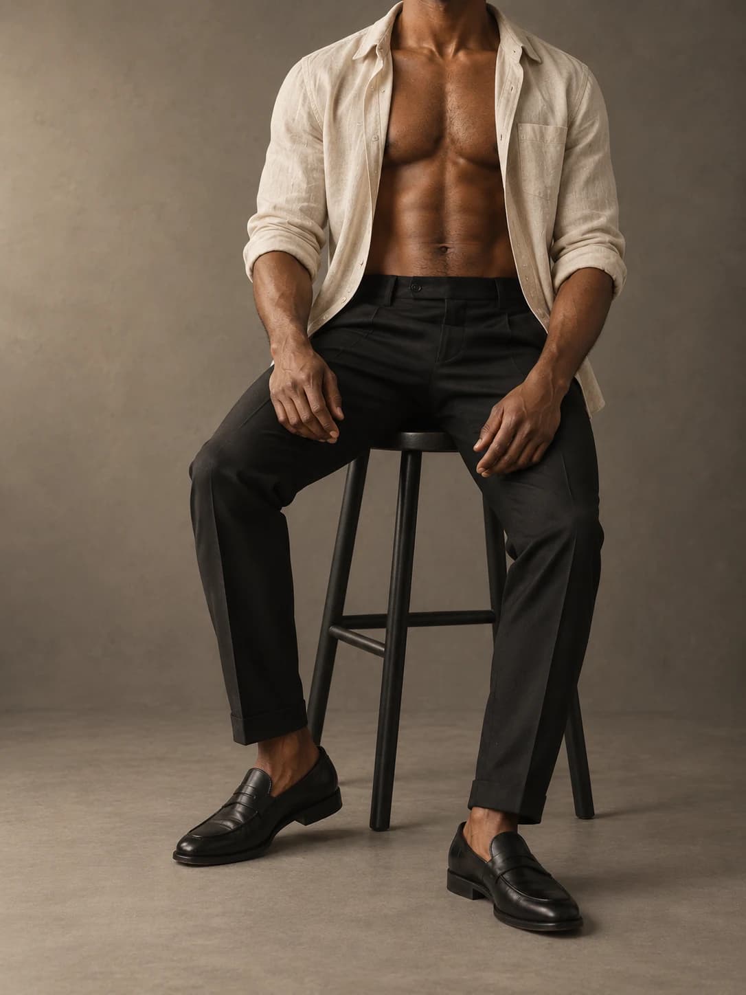 Generated studio photograph of the same fictional Amari seated in an open ecru linen shirt and black trousers, face completely outside the frame.